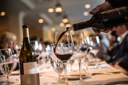 Pouring red wine into glasses at a wine club event.