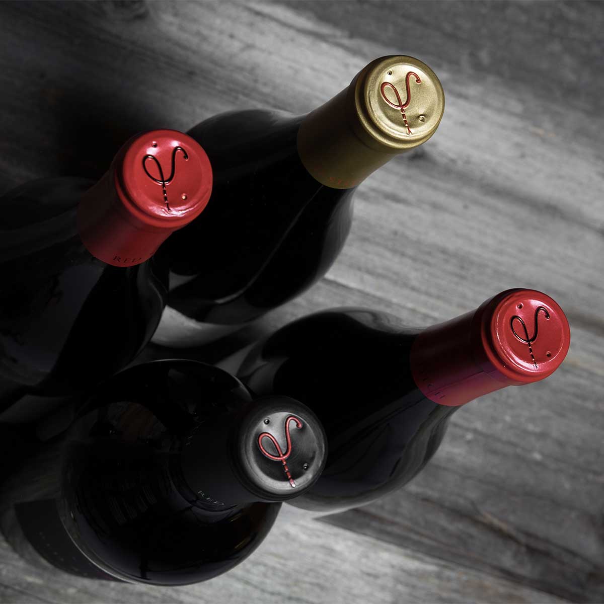 Red Stitch Wine bottles with gold and red caps, arranged on a rustic wooden table.